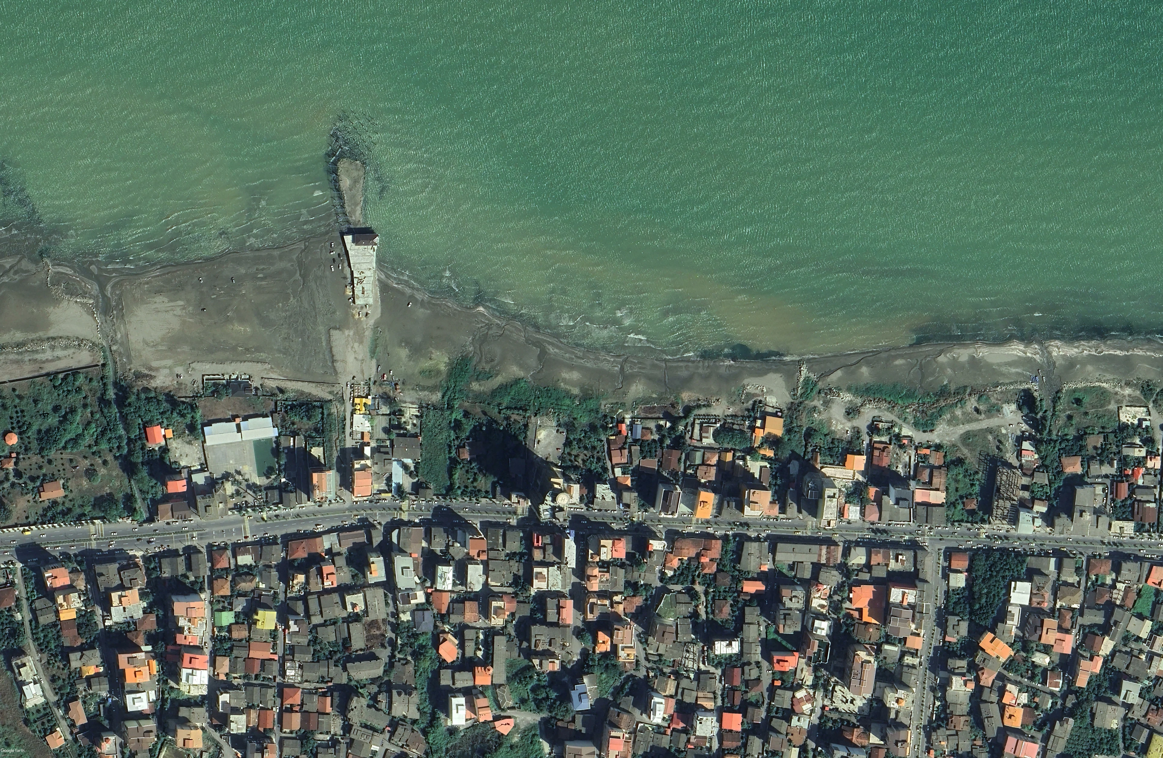 Satellite view of the tower standing on the waterline, the town set back behind the coast road